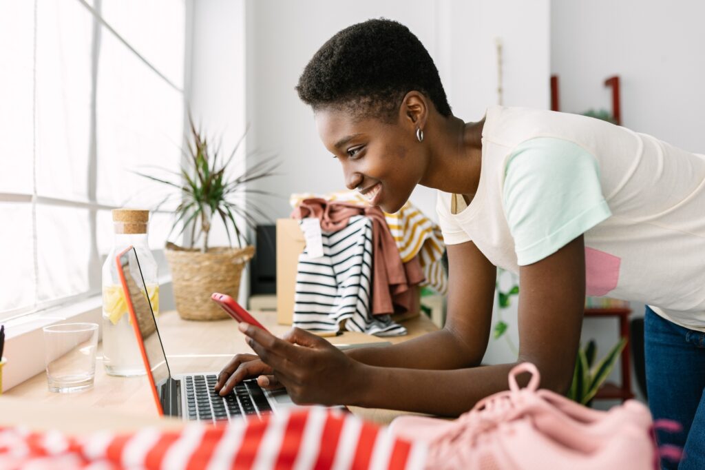 Small business african owner woman with mobile phone working on laptop in office