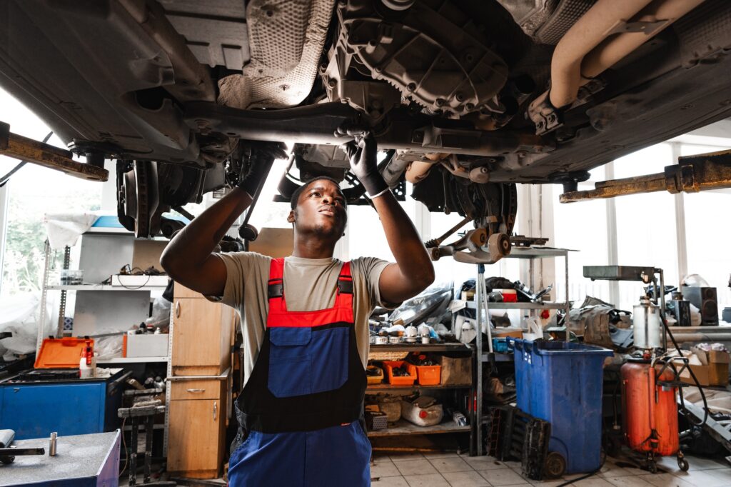 Young African mechanic in uniform working under the car in car service center